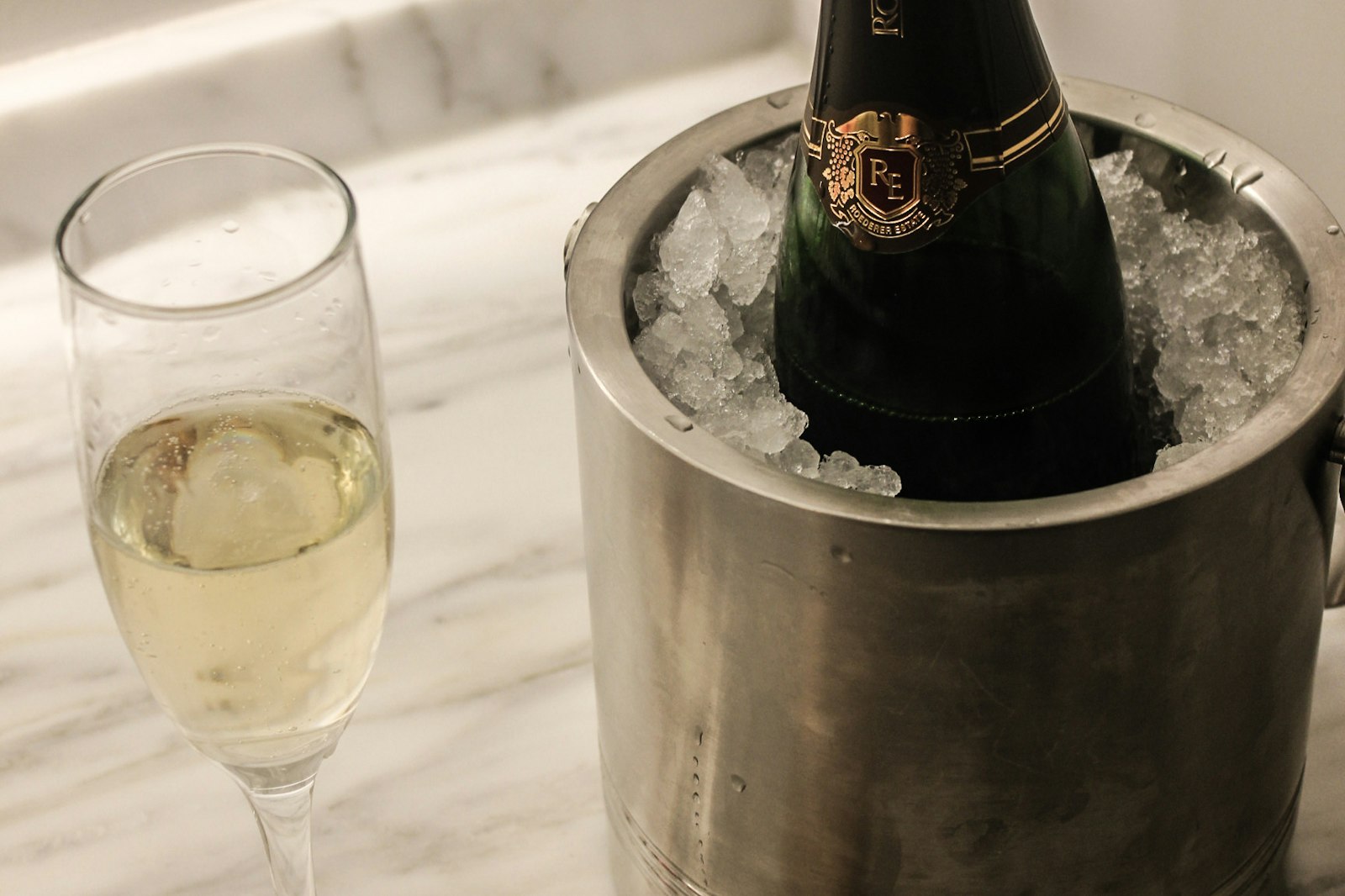 Chilled bottle in a silver ice bucket beside a poured flute on a marble surface